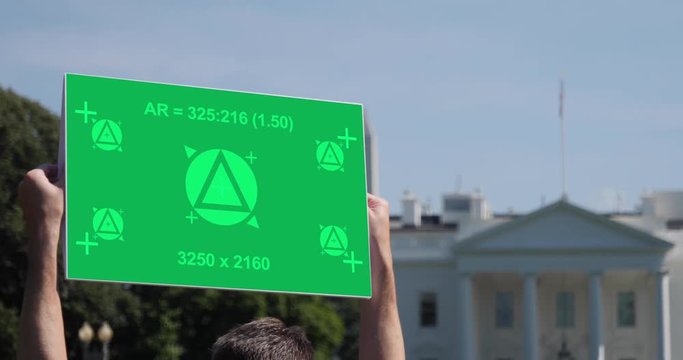 A man holds a blank green screen protest sign outside The White House in Washington, D.C. Tracking points included for custom sign message. The Washington Monument seen in the distance.  	