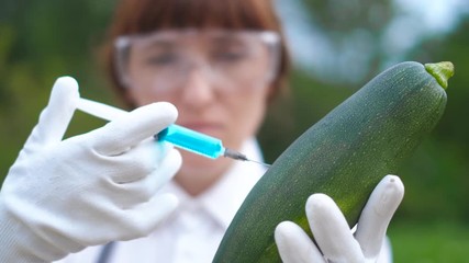 GMO scientist injecting liquid from syringe into zucchini - genetically modified food concept
