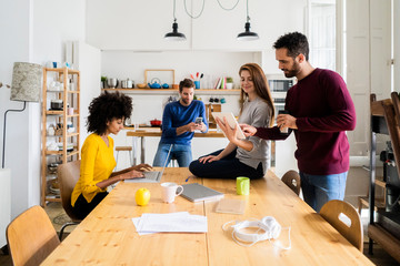 Four friends in dining room at home with portable devices
