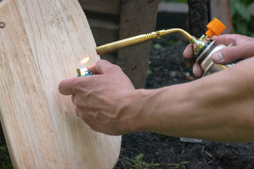 The worker is burning down by a gas burner a wooden surface to create texture.