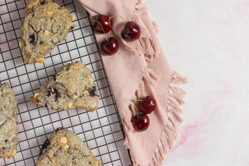 cherry and white chocolate scones on a black baking rack and pink marble background with a napkin and cherries