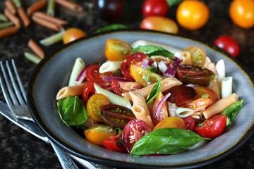 pasta salad with cherry tomatoes of different colors, colored pasta and basil. bright summer salad.