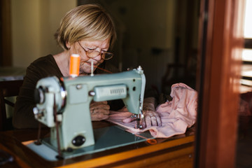 Senior woman using an sewing old machine at home