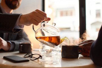 Close up. Man in a suit pouring tea into a cup in coffee shop.