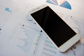 Smartphone with blank screen on background of financial reports
