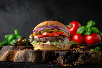 Tasty grilled burger with beef, cheese, vegetables Delicious grilled hamburger on a dark...