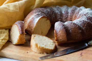 The round sweet cake strewed with icing sugar on a wooden board with a knife. 