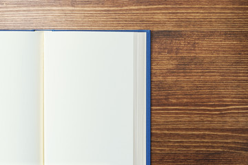 Blank white open book pages. Blue book on dark wooden table. Top view.