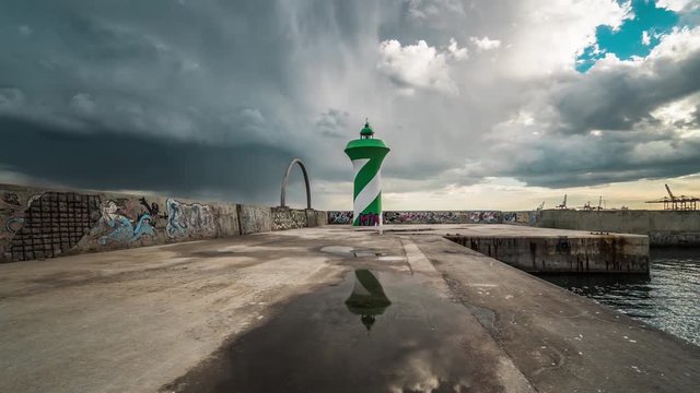 Barcelona lighthouse on breakwater wall at entrance to Barcelona port, Time lapse. Tower painted with green and white stripes.