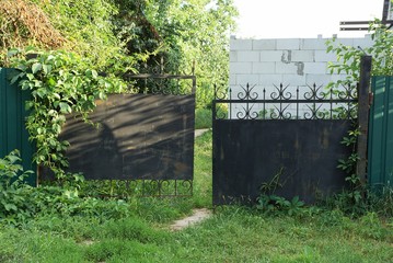old black metal gates overgrown with green vegetation and grass