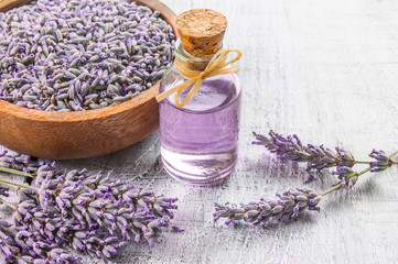 Glass bottle of Lavender essential oil with fresh lavender flowers and dried lavender seeds on white wooden rustic table, aromatherapy spa massage concept. Lavendula oleum