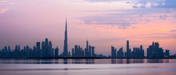 Foto op Canvas Prachtig uitzicht op het silhouet van de skyline van Dubai tijdens zonsondergang met de prachtige Burj Khalifa en vele andere gebouwen en wolkenkrabbers. Zijdezacht water stroomt op de voorgrond. © Travel Wild