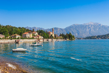 Fototapeta premium Panorama landscape on beatiful Lake Como in Tremezzina, Lombardy, Italy. Scenic small town with traditional houses and clear blue water. Summer tourist vacation on rich resort with nice harbour