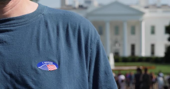 A man puts an I Voted sticker on his shirt while standing in front of The White House in Washington, D.C.  	