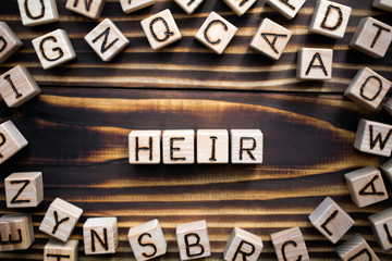 Obraz premium word heir composed of wooden cubes with letters, someone who continues or receive money property or a title concept, scattered around the cubes random letters, top view on wooden background