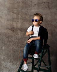 Cute stylish boy sitting on chair near concrete wall