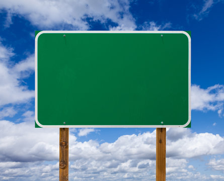 Blank Green Road Sign with Wooden Posts Over Blue Sky and Clouds