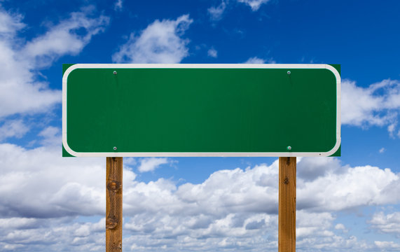 Naklejki Blank Green Road Sign with Wooden Posts Over Blue Sky and Clouds