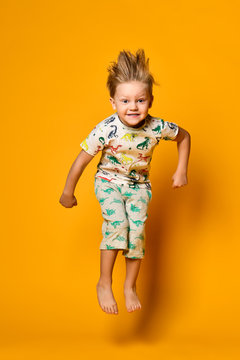 Little cute blond boy preschooler in pajamas with dinosaurs having fun has joy in the studio over yellow background.