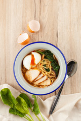 Chicken noodle soup with chicken broth, chicken fillet slices, spinach and hard boiled egg, served on a white wooden table with ingredients on it ? a perfect comfortable food