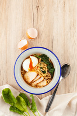 Chicken noodle soup with chicken broth, chicken fillet slices, spinach and hard boiled egg, served on a white wooden table with ingredients on it ? a perfect comfortable food