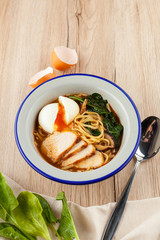 Chicken noodle soup with chicken broth, chicken fillet slices, spinach and hard boiled egg, served on a white wooden table with ingredients on it ? a perfect comfortable food