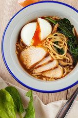 Chicken noodle soup with chicken broth, chicken fillet slices, spinach and hard boiled egg, served on a white wooden table with ingredients on it ? a perfect comfortable food