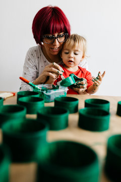 Mother and daughter doing crafts at home, painting cardboard rolls to make a Christmas tree