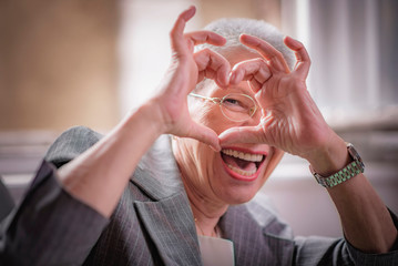 Old business lady forming a heat and smiling sincerely, sharing love