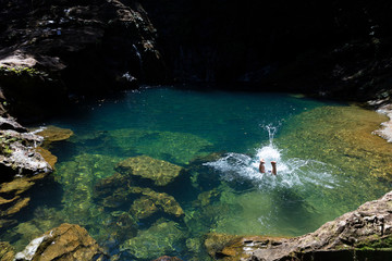 uma pessoa mergulhando dentro de lago de cor verde com cachoeira na sombra
