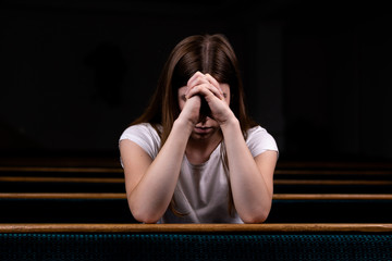 A Sad Christian girl in white shirt is sitting and praying with humble heart in the church