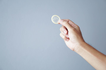 Close up man hand holding condom with grey background, health care and medical concept