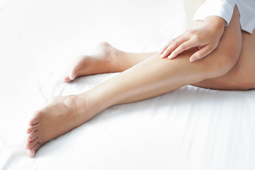 Closeup woman legs on white bed with over light form window, beauty and skin care concept, selective focus