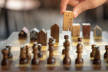 Hand of business man moving chess to Building and house models in chess game, competition success...