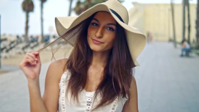 Pretty woman wearing white dress and pamela hat walking over the beach terrace at sea. Happy summer vacation