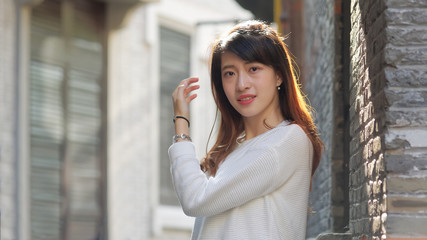 Portrait of beautiful young Chinese woman in white sweater smiling and looking at camera in Shanghai Xintiandi. People, beauty and lifestyle concept.