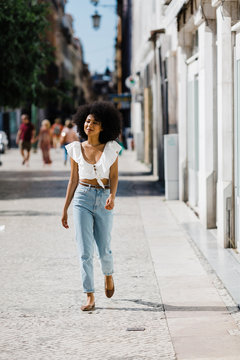 Attractive trendy woman in jeans and crop top enjoying walk on summer day on blurred urban background