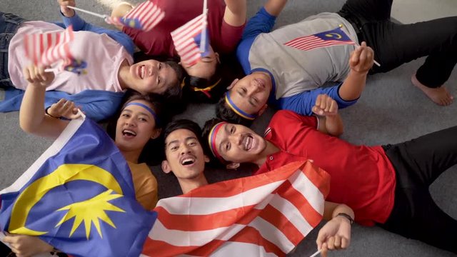 excited asian young supporter holding malaysia flag over isolated background