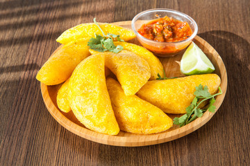 Colombian empanada with spicy sauce on wooden background