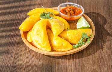 Colombian empanada with spicy sauce on wooden background