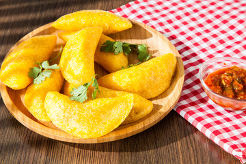 Colombian empanada with spicy sauce on wooden background