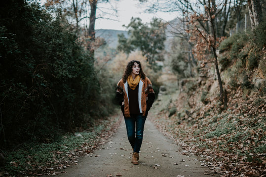 Attractive woman in warm jacket walking in autumn forest and enjoying landscape
