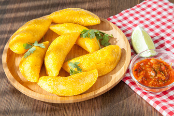 Colombian empanada with spicy sauce on wooden background