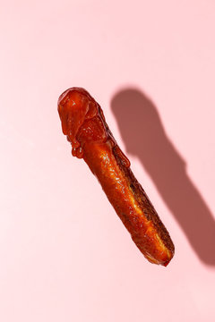delicious grilled sausage full of ketchup in a pink background