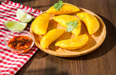 Colombian empanada with spicy sauce on wooden background