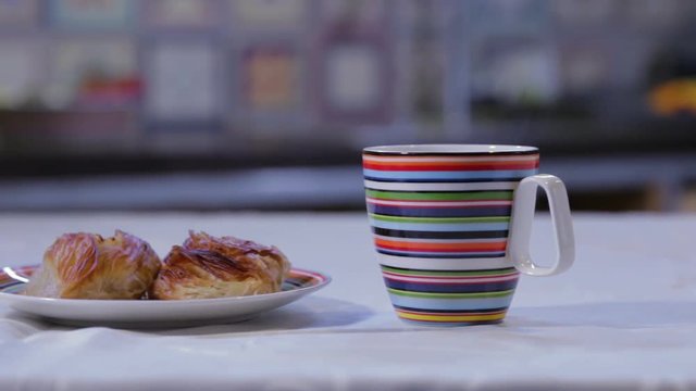 DOLLY SHOT OF MALTESE PASTIZZI PASTRY AND A COLOURFUL MUG BEING PUT NEAR THEM