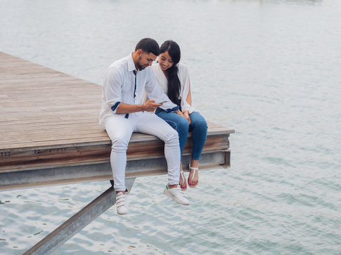 Young couple sitting and having fun taking using a phone sitting on dock