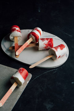 Several watermelon and cream popsicles laying on fancy dishes on dark background