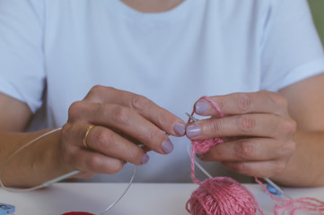 Obraz na płótnie Canvas girl knits yarn with knitting needles and crochet at home. in a white t-shirt. hand knits