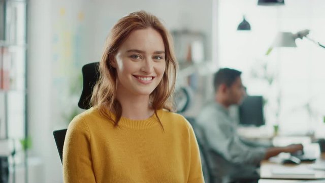 Portrait of Beautiful Young Woman with Red Hair Wearing Yellow Sweater Smiling at Camera Charmingly. Successful Woman Working in Bright Diverse Office